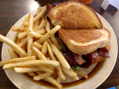 A plate with a bacon sandwich on toasted bread and a side of golden French fries.