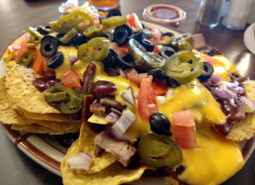 A plate of nachos topped with cheese, olives, jalapeños, tomatoes, onions, and pieces of meat.