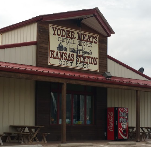 Sign for Yoder Meats and Kansas Station Gift Shop on a rustic building with picnic tables outside.
