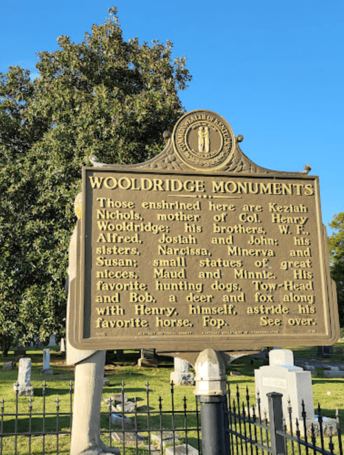 A historical marker detailing the Wooldridge Monuments and names of family members, set in a cemetery with trees.