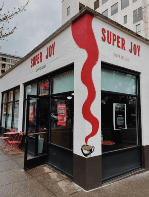 Exterior of Super Joy Coffee Lab, featuring a red coffee cup mural and large windows, with outdoor seating.