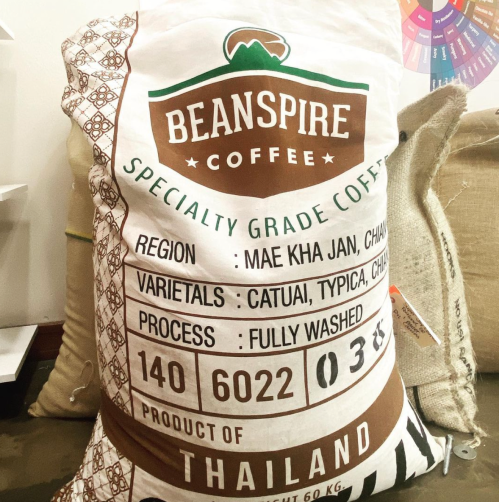 A burlap coffee sack labeled "Beanspire Coffee," detailing its origin, varietals, and processing information.