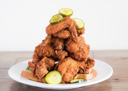 A plate stacked high with crispy fried chicken wings and garnished with cucumber slices on toasted bread.