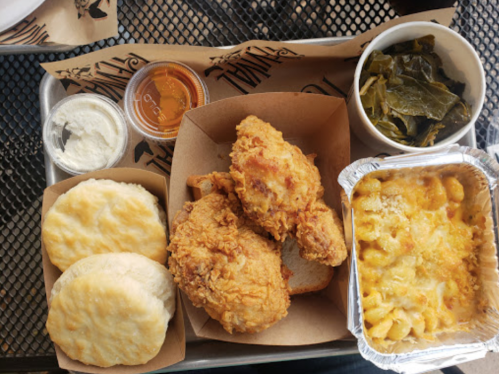 A tray of fried chicken, biscuits, macaroni and cheese, collard greens, and a small container of honey.
