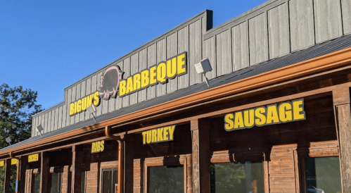 Signage for Bigu's Barbeque featuring ribs, turkey, and sausage, set against a clear blue sky.