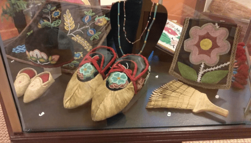 Display case featuring traditional embroidered shoes, a decorative fan, and beaded jewelry.
