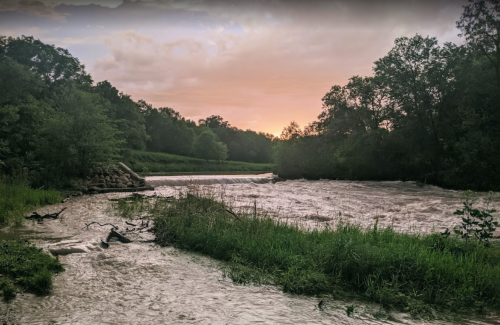 A serene river flows through lush greenery under a colorful sunset sky.