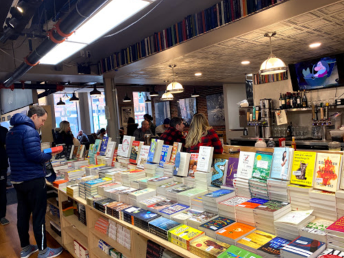 A cozy bookstore with shelves of books, a bar area, and customers browsing and enjoying the space.