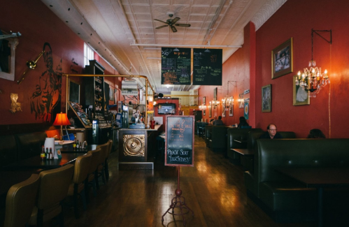 A cozy restaurant interior with red walls, booths, and a chalkboard menu, featuring warm lighting and decorative art.