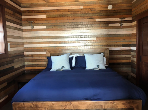 Cozy bedroom featuring a wooden bed with blue bedding and striped wooden walls. Two pillows on the bed.