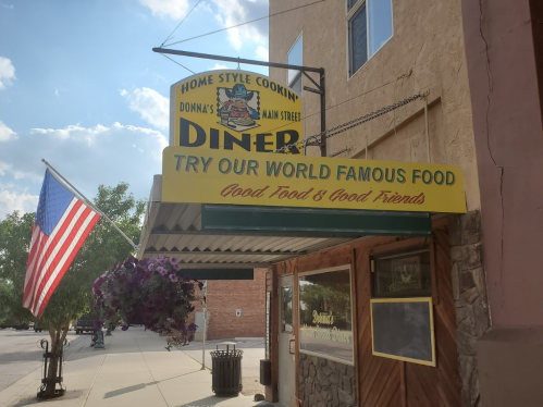 A diner with a sign reading "Home Style Cookin' - Try Our World Famous Food" and an American flag outside.