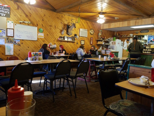 A cozy diner interior with wooden walls, tables, and patrons enjoying meals. Condiments are visible on the tables.
