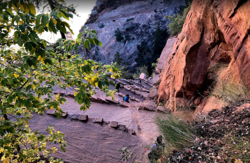 A winding stone path leads through a rocky landscape, surrounded by greenery and steep cliffs.