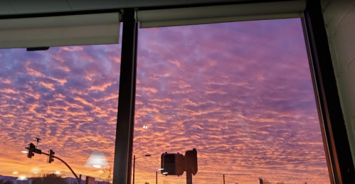 A vibrant sunset with purple and orange hues, viewed through a window with silhouettes of traffic lights and street signs.