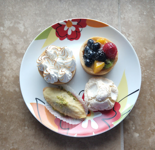 A colorful plate with four assorted desserts: meringue, fruit tart, and two cream-filled pastries.