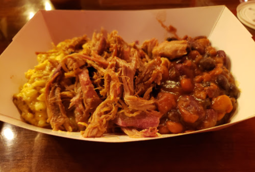 A takeout box filled with pulled pork, macaroni and cheese, and baked beans.
