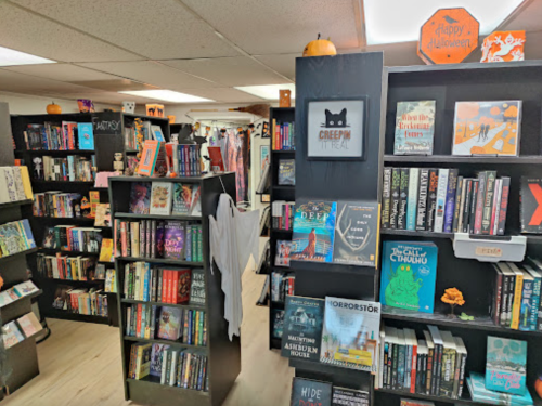 A cozy bookstore with shelves filled with books, Halloween decorations, and a sign that says "Happy Halloween."