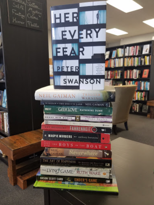A stack of books with "Her Every Fear" by Peter Swanson on top, surrounded by various titles by Neil Gaiman and others.