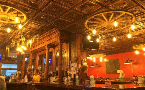 Cozy restaurant interior with wooden bar, vintage decor, and warm lighting from hanging fixtures.