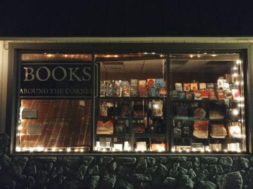A cozy bookstore window displaying various books, illuminated by warm lights.