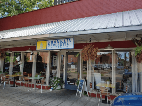 Exterior of Franklin Mercantile Deli with a blue sign, outdoor seating, and a welcoming open door.