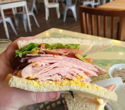 A hand holding a cross-section of a sandwich filled with layers of ham, lettuce, tomato, and mustard on white bread.