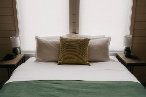 A neatly made bed with white linens, a green throw, and decorative pillows, flanked by two bedside lamps.