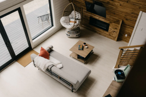 A cozy living room with a gray sofa, wooden accents, a hanging chair, and a record player, viewed from above.