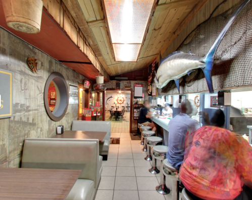 A cozy diner interior with booths, a bar, and a large fish mounted on the wall, featuring patrons enjoying their meals.
