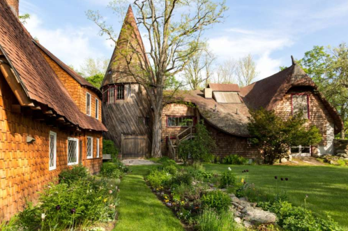 A whimsical house with a conical tower, surrounded by lush greenery and colorful flowers in a serene garden setting.