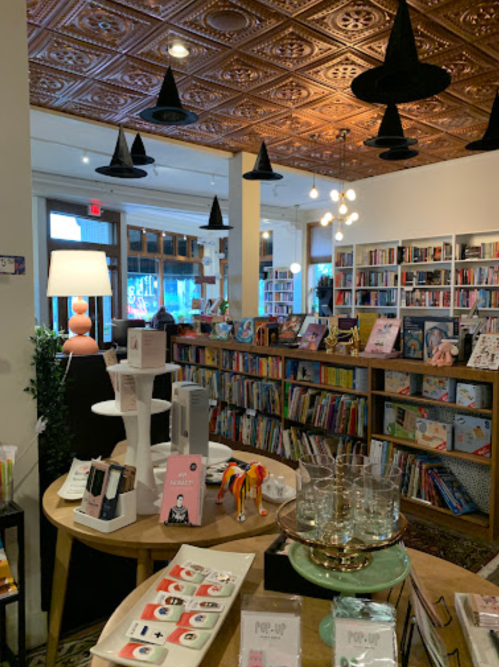 A cozy bookstore interior with bookshelves, a round table displaying items, and unique ceiling lights.