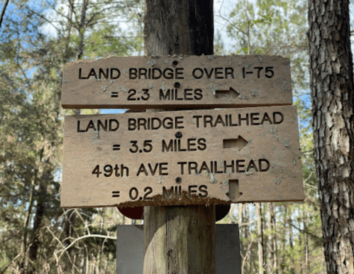 Wooden signpost with trail distances: Land Bridge Over I-75 (2.3 miles), Land Bridge Trailhead (3.5 miles), 49th Ave Trailhead (0.2 miles).