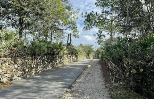 A scenic pathway lined with stone walls and lush greenery, leading through a tranquil outdoor setting.