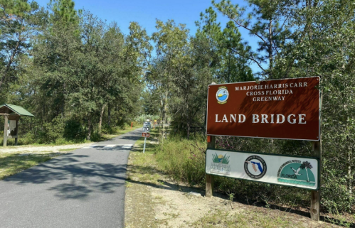 Sign for "Land Bridge" along a paved path in a wooded area, part of the Marjorie Harris Carr Cross Florida Greenway.