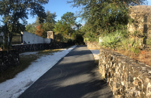 A peaceful pathway lined with stone walls and greenery, leading through a sunny, wooded area.