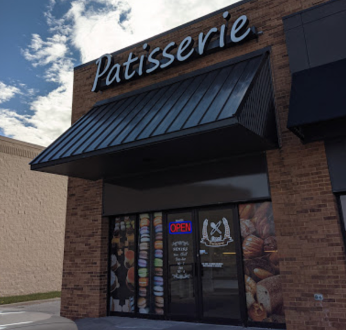 Exterior of a patisserie with a large sign, open door, and a display of pastries in the window.