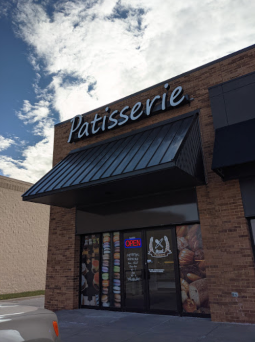 A storefront with a sign reading "Patisserie" and an illuminated "Open" sign, featuring pastry images on the door.