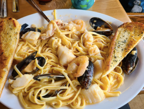 A plate of seafood pasta with shrimp, scallops, and mussels, served with two slices of garlic bread.
