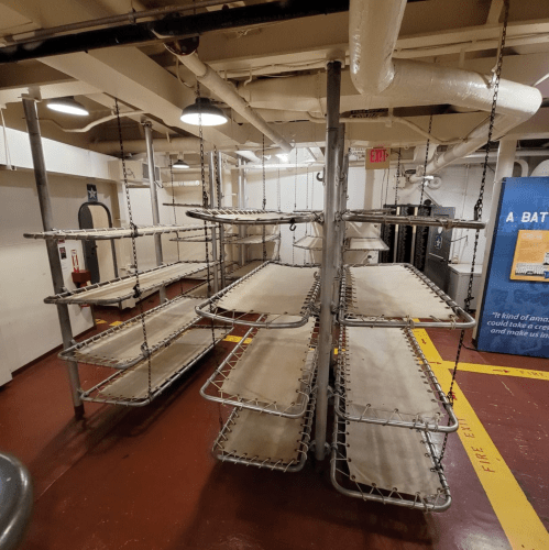 A series of metal bunk beds arranged in a room with industrial decor and pipes overhead.