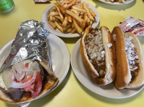 A plate with a wrapped sandwich, two hot dogs topped with onions, and a side of fries.