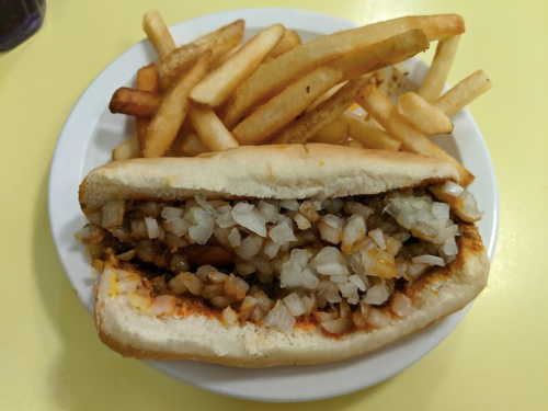 A plate with a sandwich filled with chopped meat and onions, accompanied by a side of golden French fries.