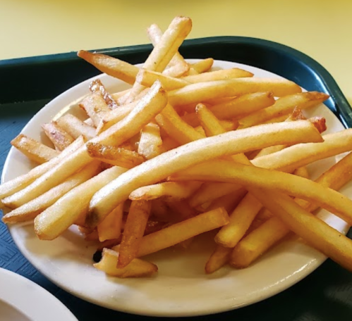 A plate of golden, crispy French fries piled high on a white dish.