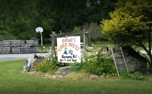 Sign for Apgar's Cider Press in Harmony, NJ, surrounded by greenery and wooden crates in the background.