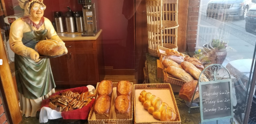 A bakery display featuring various loaves of bread and pastries, with a decorative figure holding a loaf.