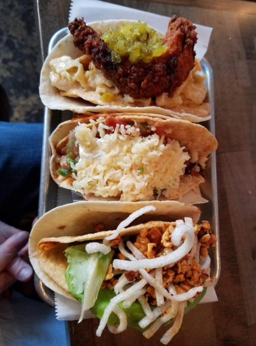 A tray with four tacos, each filled with different ingredients, including fried chicken, rice, and toppings.