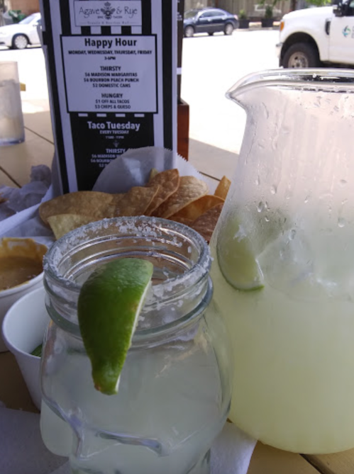 A table with drinks, chips, and a menu for happy hour at Agave & Rye, featuring margaritas and snacks.