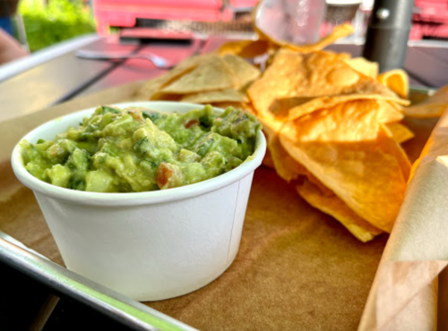 A cup of guacamole next to a pile of tortilla chips on a tray.