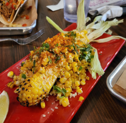 A vibrant plate of elote topped with cheese, spices, and herbs, served with a lime wedge.