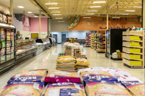 A spacious grocery store aisle with shelves of products, bags of rice, and a display of refrigerated items.