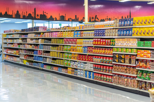 A brightly lit grocery aisle filled with various packaged food products against a colorful skyline mural.